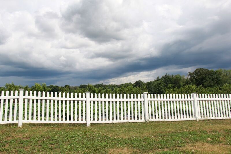 White vinyl straight picket fence along a field under a storm sky