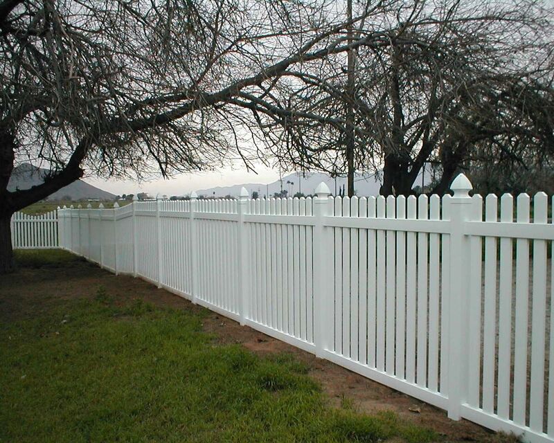 White vinyl five-foot picket fence running along a field at dusk