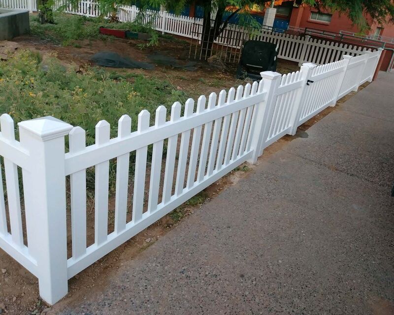 White vinyl scalloped picket fence and walk gate along a school garden