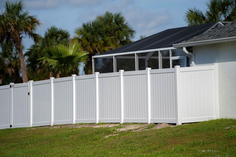 Six-foot white vinyl privacy fence with double-grooved panels beside a screened lanai