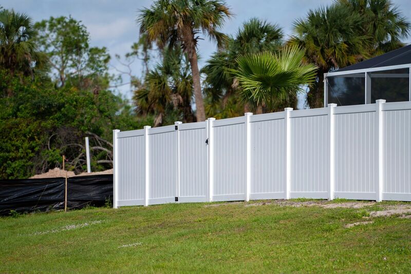 Six-foot white vinyl privacy fence and walk gate in a tropical setting