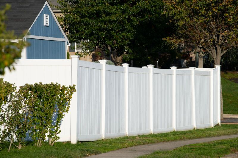 Six-foot white vinyl privacy fence running along a sidewalk beside a blue house