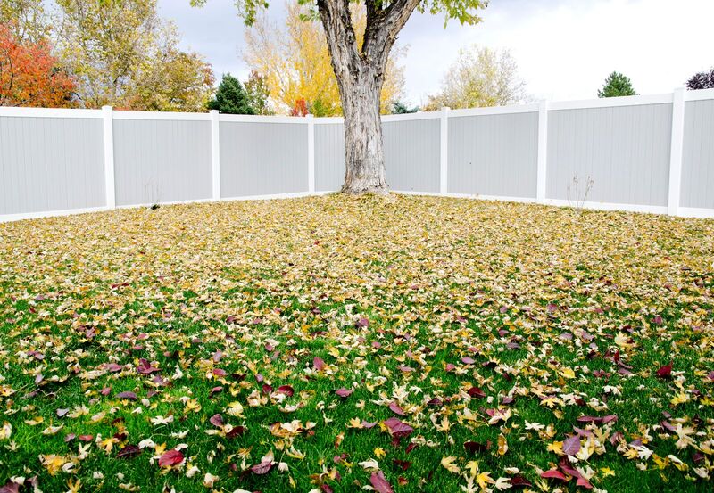 Two-tone vinyl privacy fence with gray infill and white frame around a leaf-covered yard