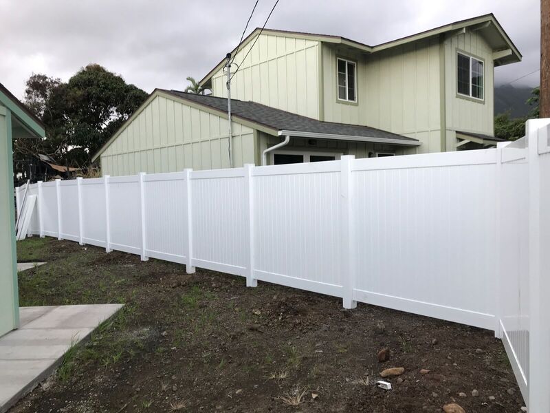 White vinyl privacy fence newly installed along a graded side yard