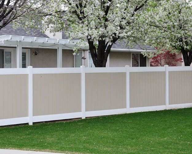 Two-tone vinyl privacy fence with tan infill and white frame beneath blossoming trees