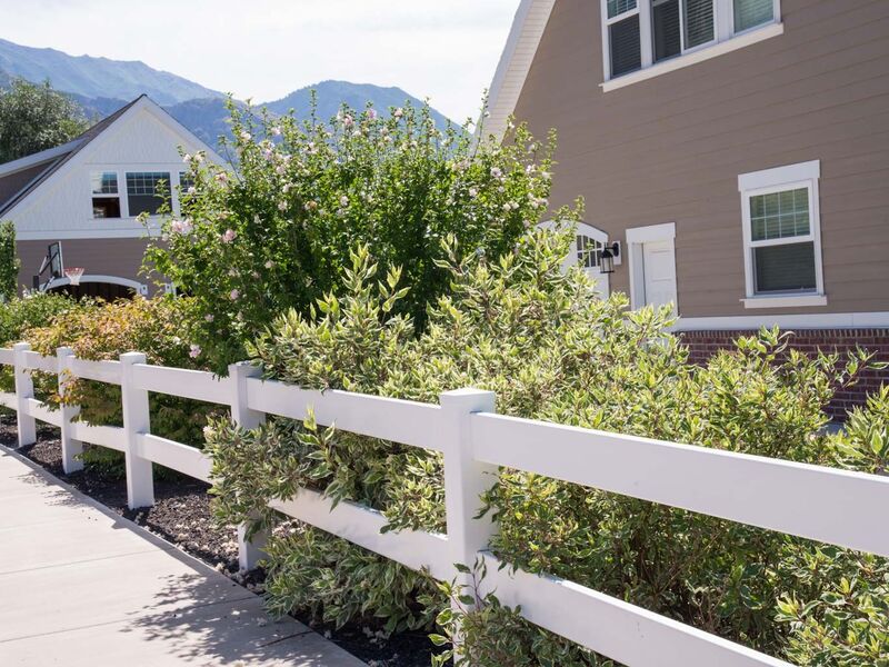 White vinyl two-rail ranch fence running along a sidewalk planting bed