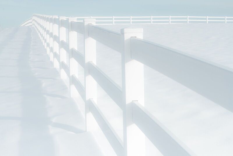 White vinyl three-rail ranch fence crossing a snow-covered field