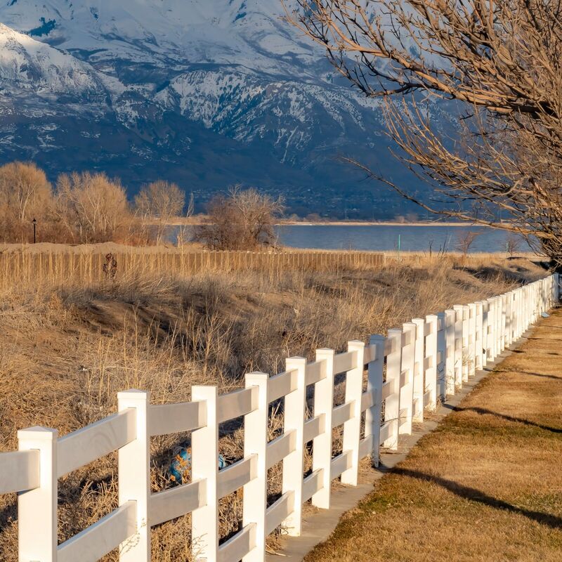 White vinyl three-rail ranch fence with snowy mountains behind