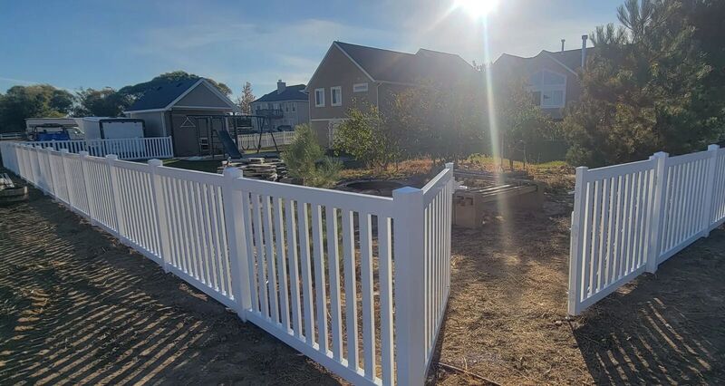 White vinyl picket fence enclosing a backyard garden at sunset
