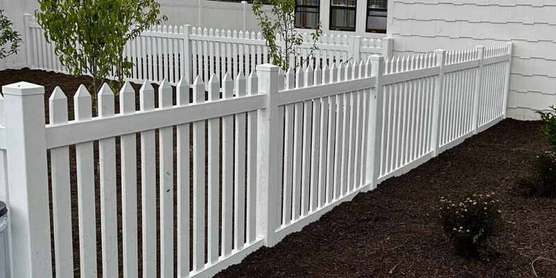 White vinyl picket fence running along a mulched planting bed