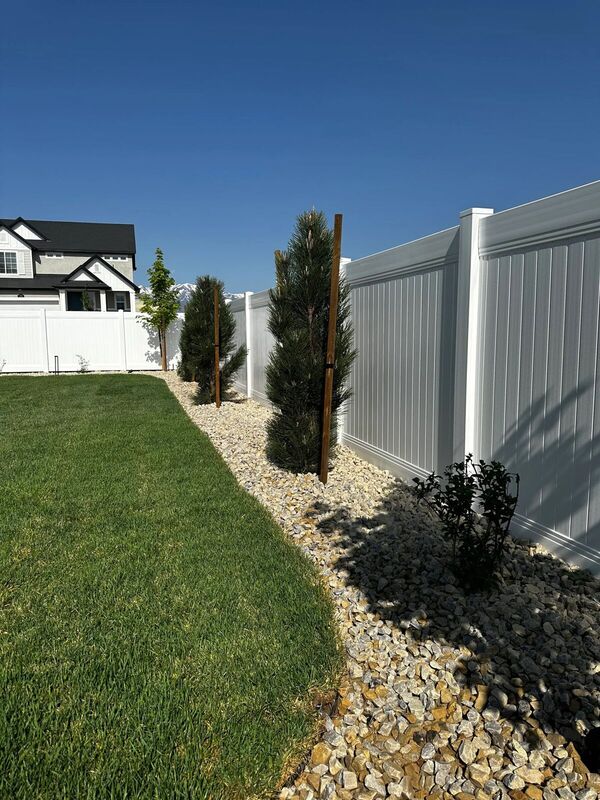 White vinyl privacy fence beside a gravel border planted with evergreens