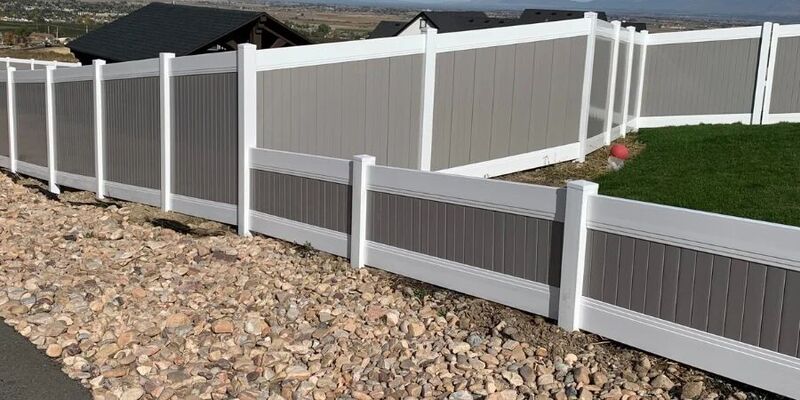 Two-tone vinyl privacy fence with gray infill and white frame stepping down a slope