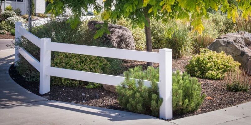White vinyl two-rail fence accenting a landscaped corner